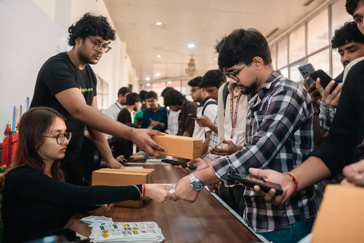 Volunteers at the registration desk handing a swag box across to participants holding up their phones to check in